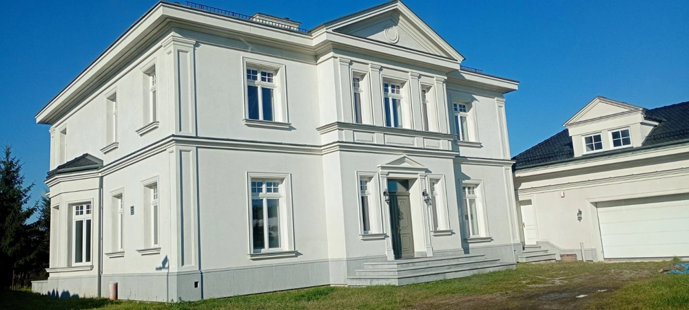 Klasyczny biały dwukondygnacyjny dom z ukończoną elewacją domu, zamontowanymi oknami i garażem