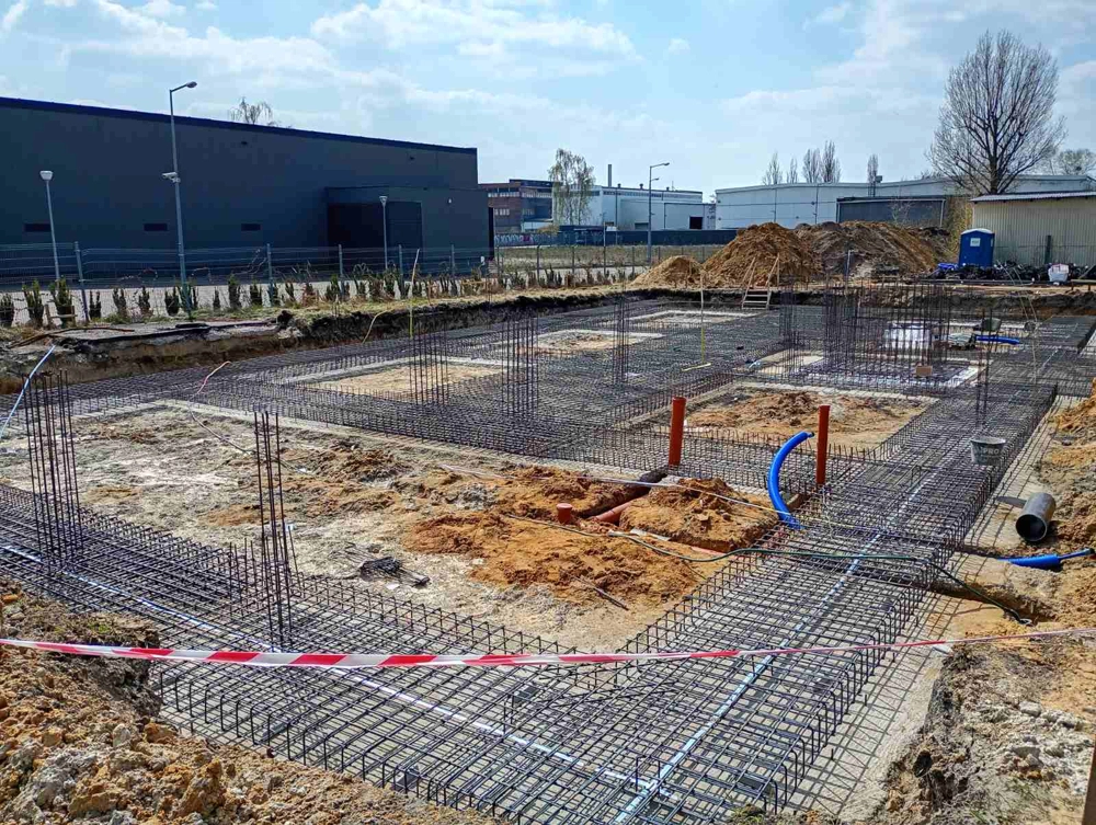Zbrojenie ław fundamentowych z widocznymi instalacjami na terenie budowy