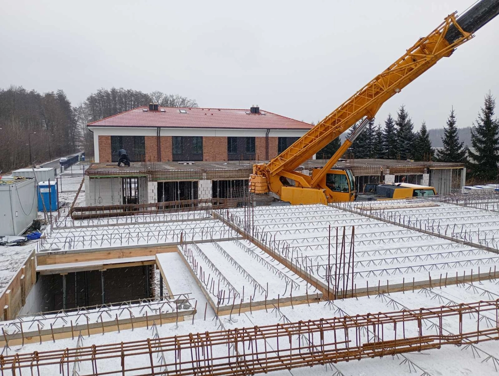 Plac budowy z montażem płyty fundamentowej z zbrojeniem i żurawiem zimą