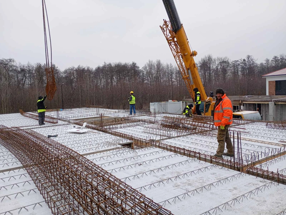 Montaż zbrojenia i prefabrykowanych dźwigarów na płycie fundamentowej z pomocą dźwigu