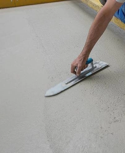 Wylewki betonu wyrównywane stalową pacą na podłodze przez pracownika, uzyskując gładką powierzchnię
