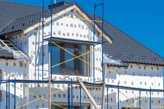 Ocieplenie budynku: montaż płyt styropianowych na ścianach i rusztowanie przy domu