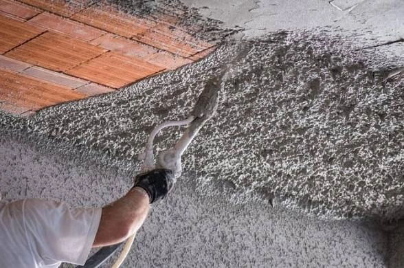 Pracownik nakłada tynk natryskowo na sufit – Tynkowanie