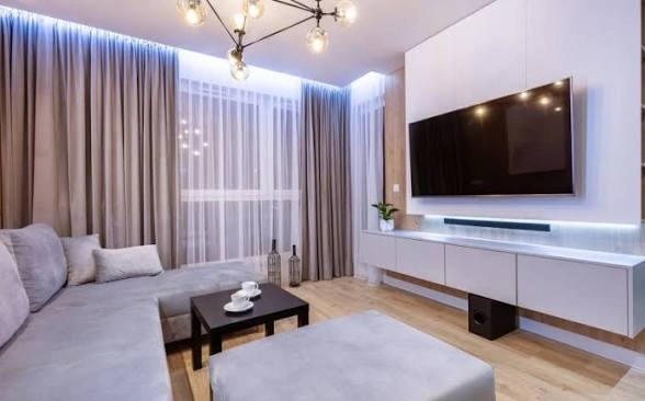 Nowoczesny salon z szarą sofą narożną, stolikiem kawowym i telewizorem ściennym, Wykończenia wnętrz
