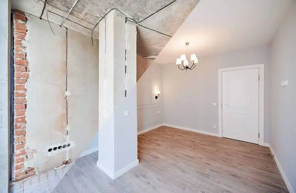 Wnętrze w stanie deweloperskim domu z gładzią na ścianach, odsłoniętymi instalacjami elektrycznymi i surowym sufitem