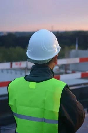 Pracownik w białym kasku i odblaskowej kamizelce podczas nadzoru budowlanego na placu budowy